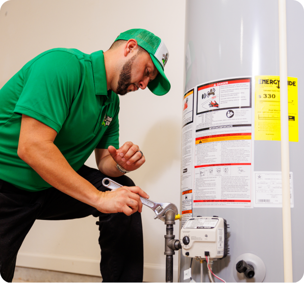 Plumber in green shirt and cap working on a water heater.